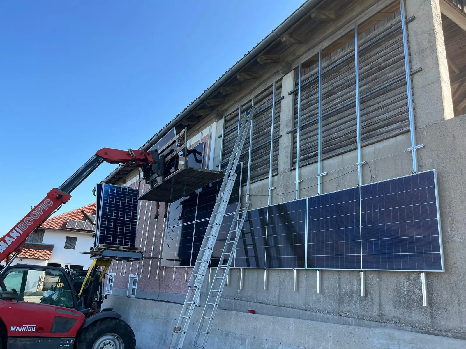 Montage von PV-Modulen an der Hallenfassade in Behamberg, Module werden per Teleskoplader angehoben