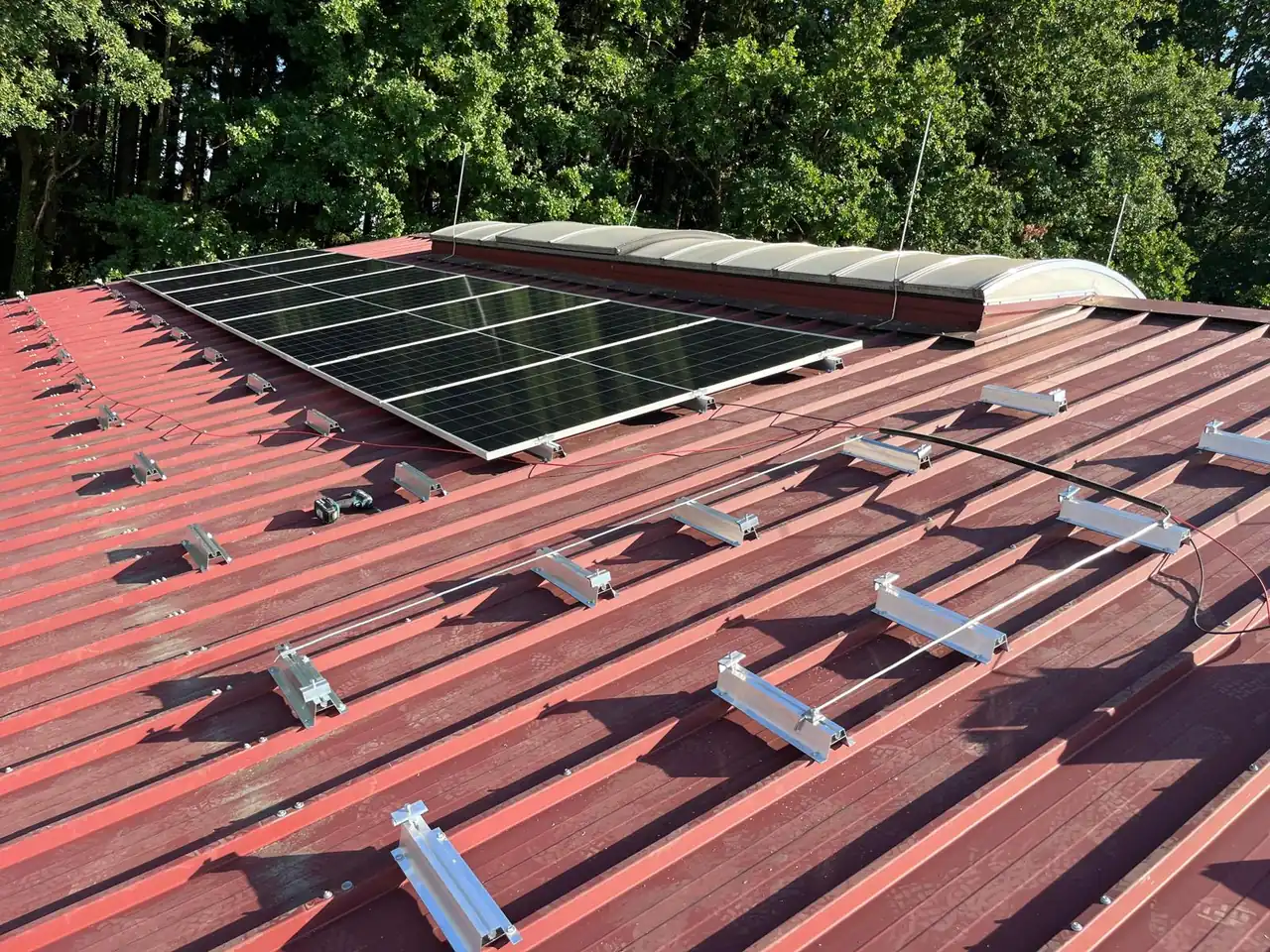 Kurzschienen und erste PV-Module auf rotem Trapezblechdach neben Lichtkuppeln