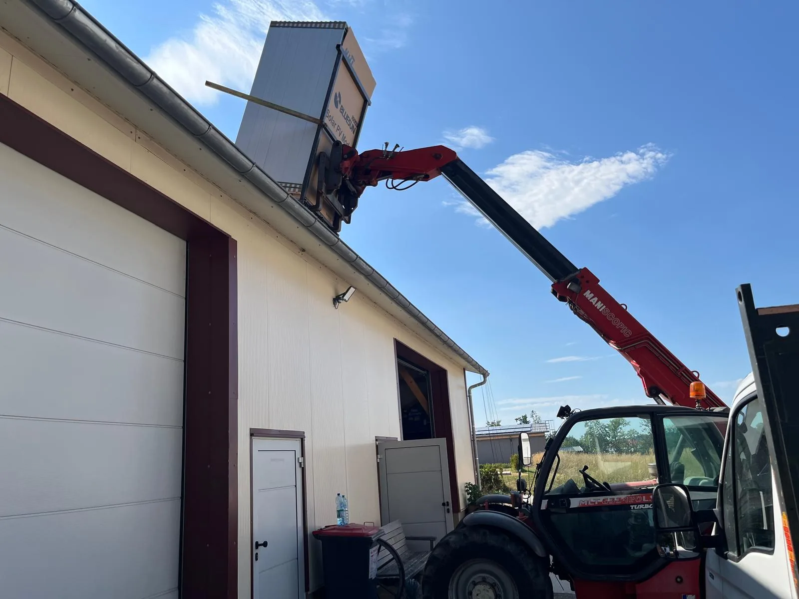 Teleskoplader hebt eine Palette PV-Module an einer Halle aufs Dach