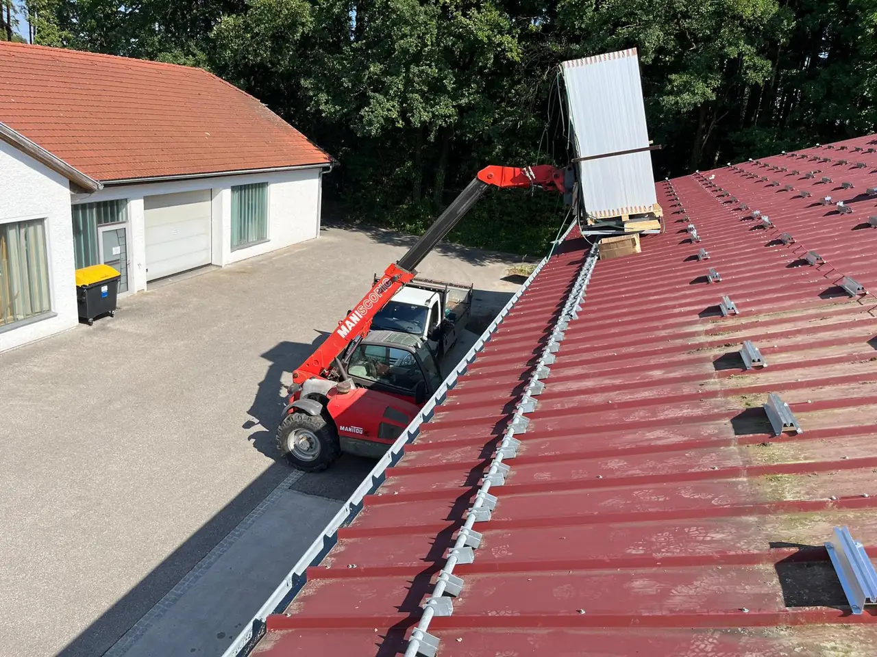 Teleskoplader hebt PV-Module auf ein Trapezblechdach mit vormontierten Kurzschienen