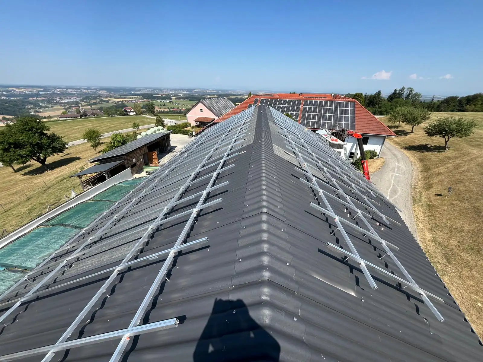 Montageschienen der PV-Unterkonstruktion auf dem dunklen Wellplattendach der Halle in Behamberg, Blick über den First auf den Hof